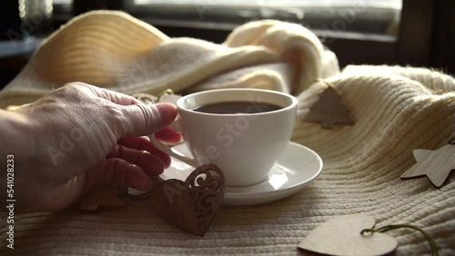 Hygge style. Woman's hand takes a mug of black coffee wrapped in a warm scarf with wooden Christmas decorations. Vintage style, still life photo