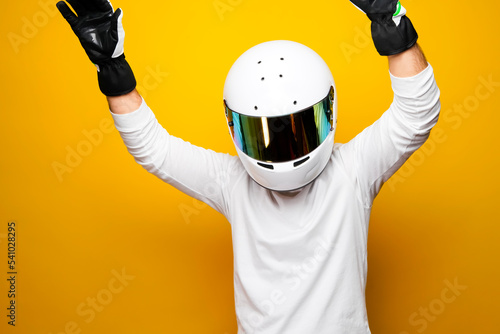 A Helmet Wearing Race Car Driver celebrating on the podium after winning the race. Male Racer on yellow background.