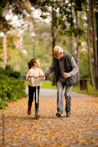 Bilde på lerret Senior man teaching his granddaughter how to ride kick scooter in park