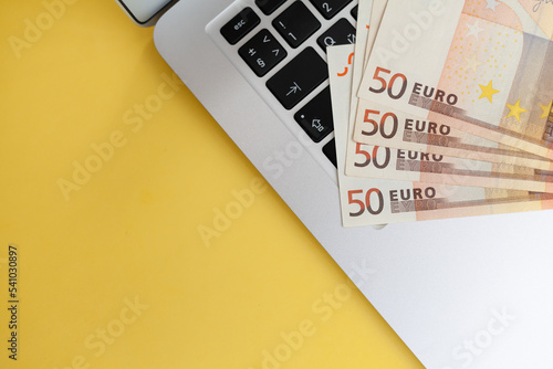 Fifty euro banknotes on a laptop background and on a yellow background, Purchases and earnings via the Internet. Cash paper currency, payment, earnings and savings, the concept of money and finance.