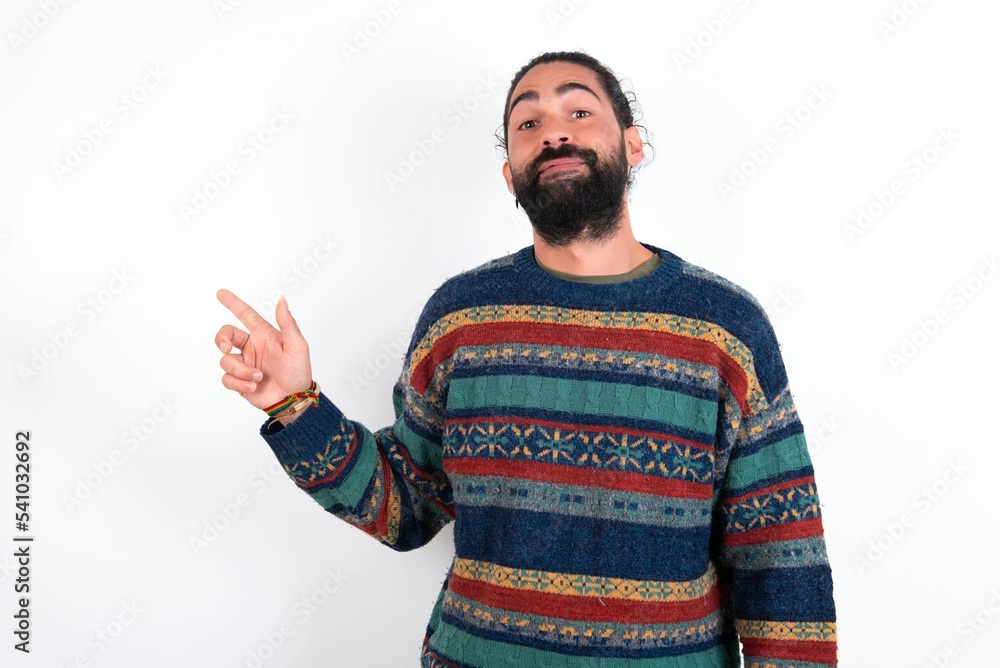 Naklejka premium Positive Caucasian man with beard wearing sweater over white background with satisfied expression indicates at upper right corner shows good offer suggests to click on link