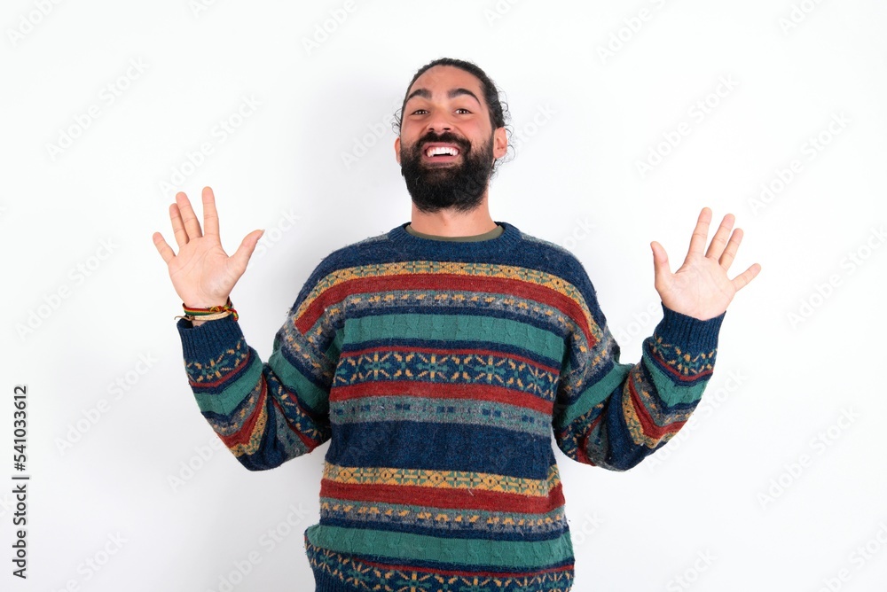 Naklejka premium Delighted positive Caucasian man with beard wearing sweater over white background opens mouth and arms palms up after having great result