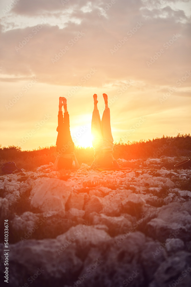 Mother and daughter practicing yoga together in sunset sunrise time in nature.