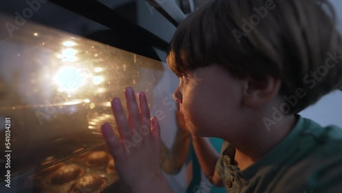 Child staring at oven. Kid looking at cookies baking inside heating stove