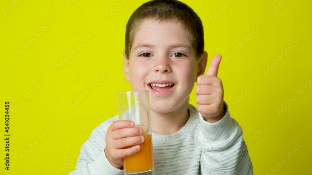 A happy child drinks orange juice and shows a thumbs up on a yellow background. A happy child drinks orange juice and shows a thumbs up on a yellow background.