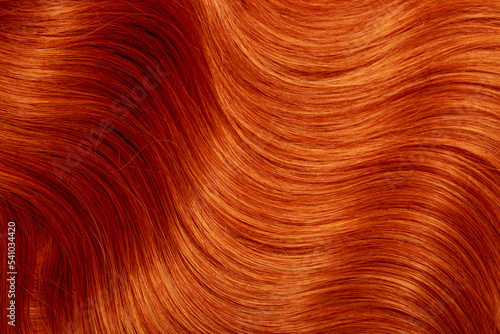 Red hair close-up as a background. Women's long orange hair. Beautifully styled wavy shiny curls. Hair coloring bright shades. Hairdressing procedures, extension.