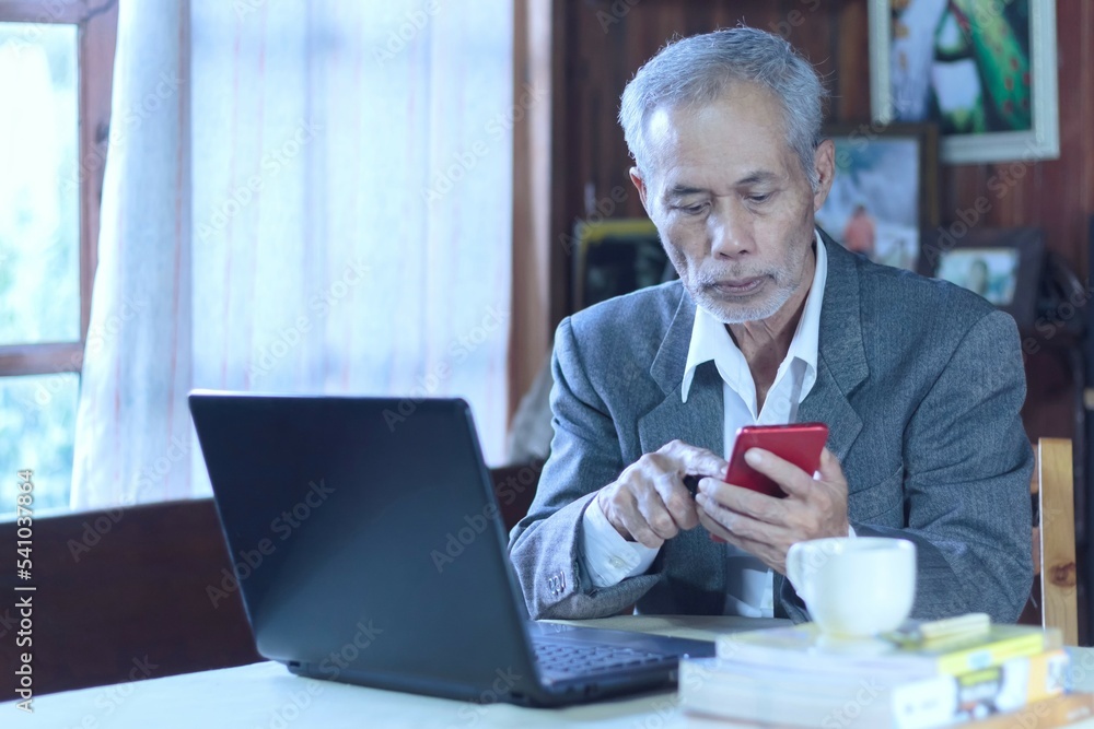 Asian senior businessman answering the phone while working from home Asian senior businessman answering the phone while working from home