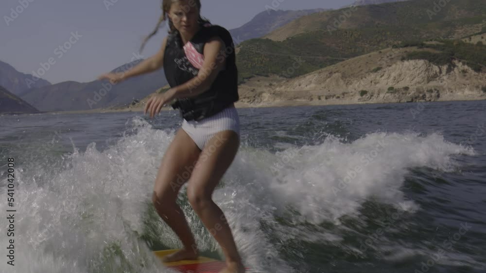 Tracking shot of woman wakesurfing on lake / Deer Creek, Utah, United States Tracking shot of woman wakesurfing on lake / Deer Creek, Utah, United States