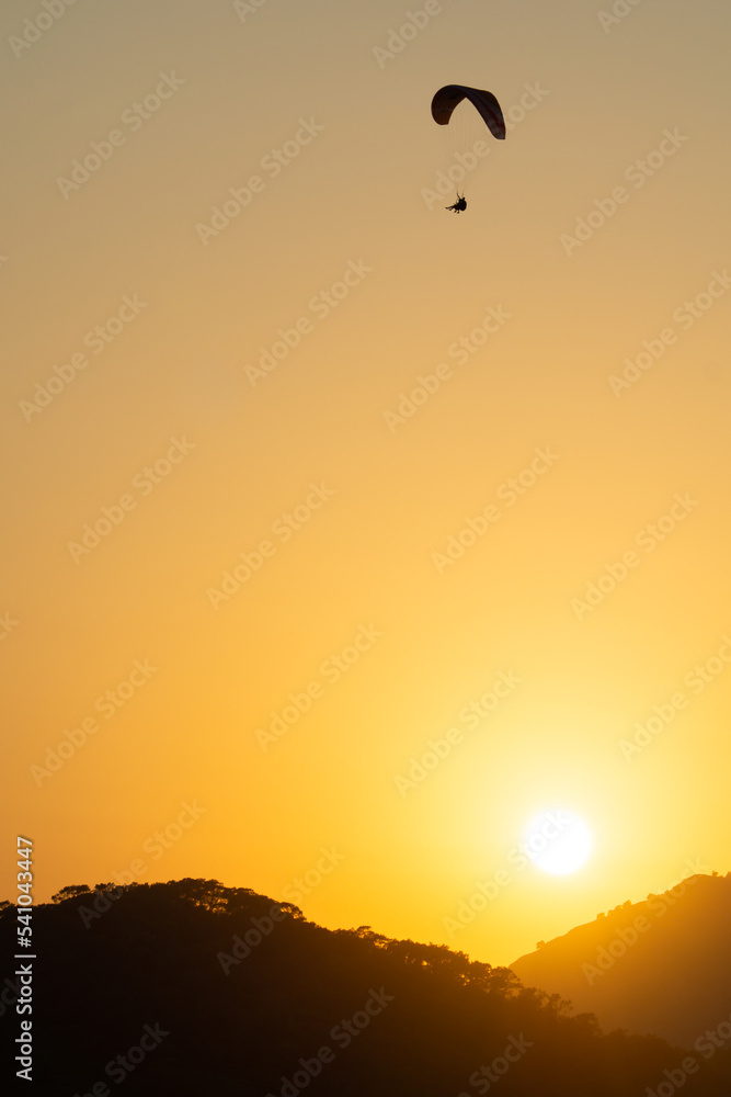 Mountainous landscape at sunset with the silhouette of a paraglider flying in the sky at sunset