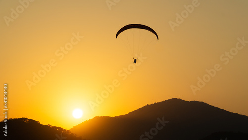 Mountainous landscape at sunset with the contrasting silhouette of a paraglider flying in the sky.