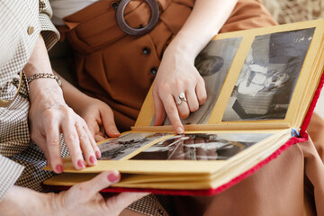 Mom and daughter are considering a family photo album. An elderly woman and young girl hold a family photo album.