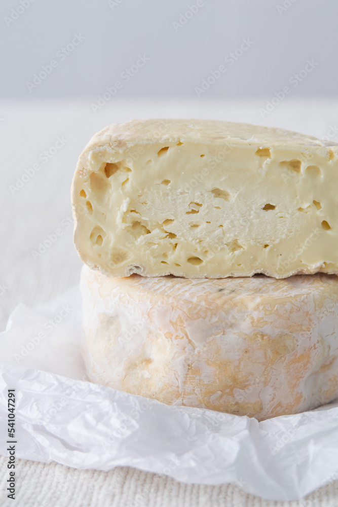 French soft strong smelling cheese Munster on white paper on light rustic background, selective focus French soft strong smelling cheese Munster on white paper on light rustic background, selective focus