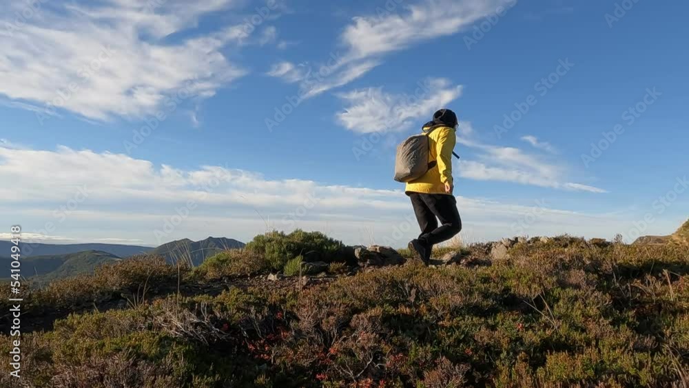 The man in the yellow jacket is walking along the mountain path at sunrise, in the background a panorama of the mountains. Recorded in slow motion. The man in the yellow jacket is walking along the mountain path at sunrise, in the background a panorama of the mountains. Recorded in slow motion.