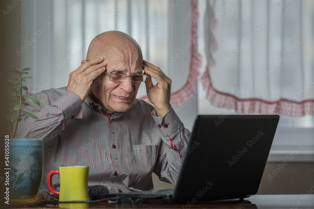 Senior man in eyeglasses touching head with hands and looking at laptop. Migraine and headache is consequence of intense work at computer. Senior man in eyeglasses touching head with hands and looking at laptop. Migraine and headache is consequence of intense work at computer.
