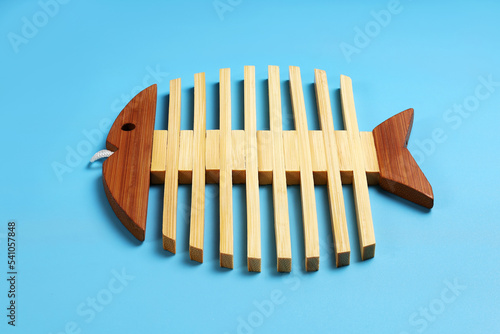 Wooden stand for hot dishes on blue surface, in shape of skeleton of fish