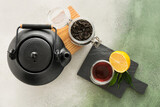 Cup of hot black tea, teapot and dried leaves on color background