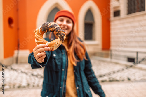 Fall tourist woman in a bright hat and autumn jacket holding baked obwarzanek traditional polish cuisine snack bagel on old city Market square in Krakow  photo