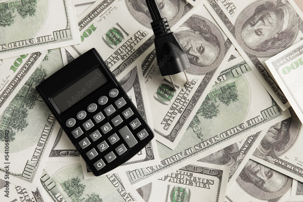 Fototapeta premium Calculator and plug on dollar banknotes. Heating season concept