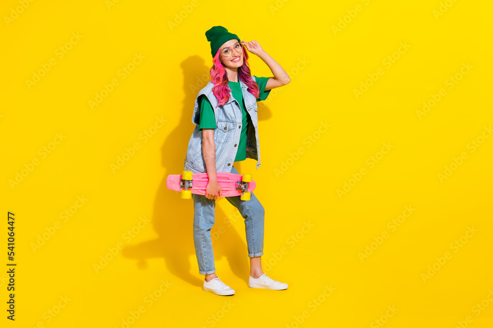 Full length photo of pretty cheerful girl dressed denim vest hand eyewear riding longboard isolated yellow color background Full length photo of pretty cheerful girl dressed denim vest hand eyewear riding longboard isolated yellow color background
