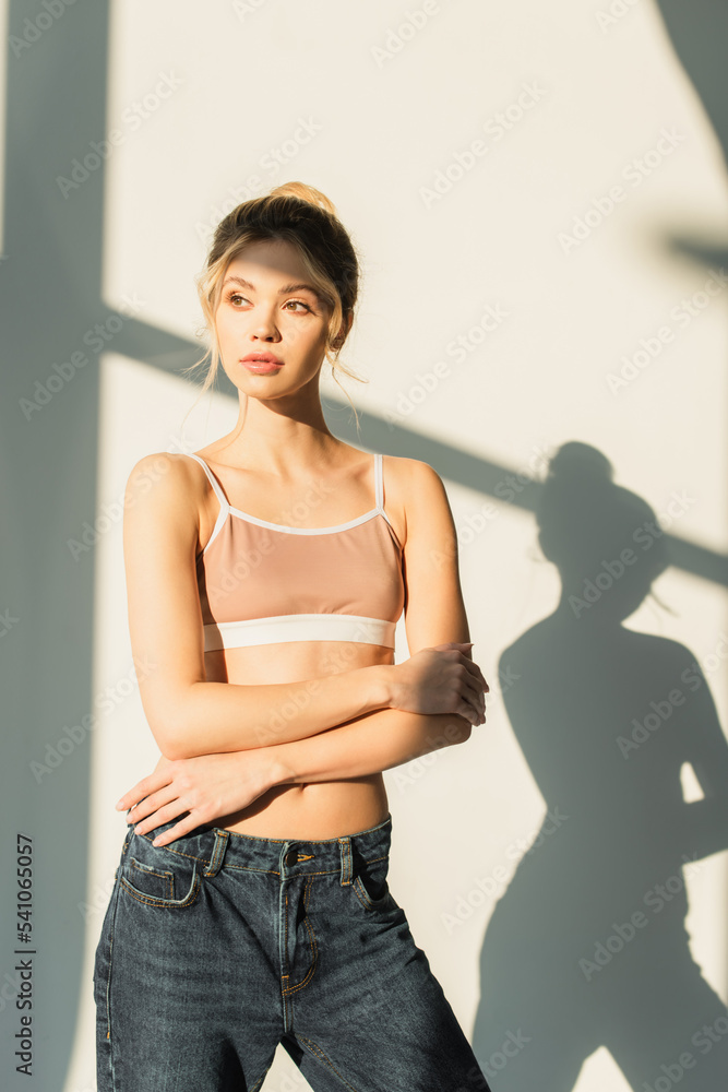 slender woman in sports top standing in light on white background with shadows