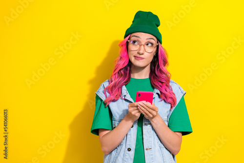 Photo of minded lady wear green hat trendy clothes look up empty space decide buy modern new gadget isolated on yellow color background