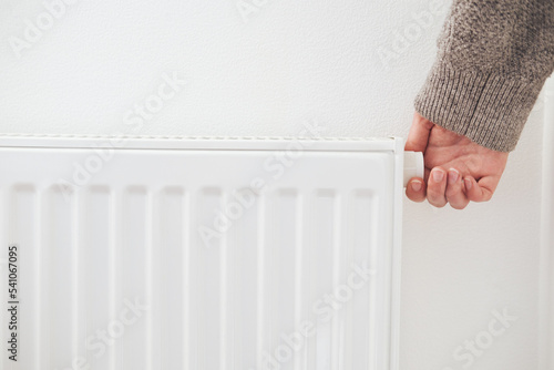 Hand turning down thermostat of a central heating radiator. Energy saving, cold winter season, reduced power consumption and economy theme.