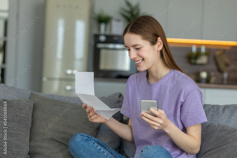 Happy young woman using mobile app to paying household bill, taxes or insurance use secure internet banking. Female holding bank letter reading good news, closed her bank loan Happy young woman using mobile app to paying household bill, taxes or insurance use secure internet banking. Female holding bank letter reading good news, closed her bank loan