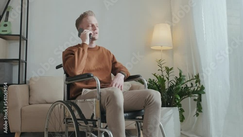 Caucasian wheelchaired man making phone call while sitting by window in his apartment photo