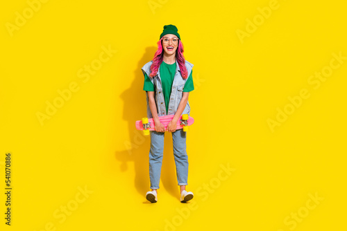 Full length photo of cheerful excited girl dressed denim vest eyewear riding longboard isolated yellow color background