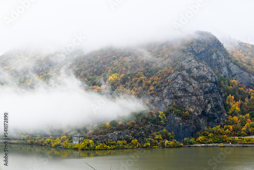 A mountain cliff breaks through the fog overlooking the Hudson River in fall during peak foliage.