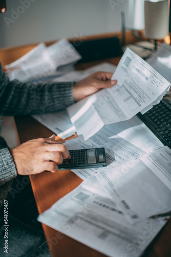 Fotografie Close-up of male hands with a utility bill, a lot of checks and a calculator on the table