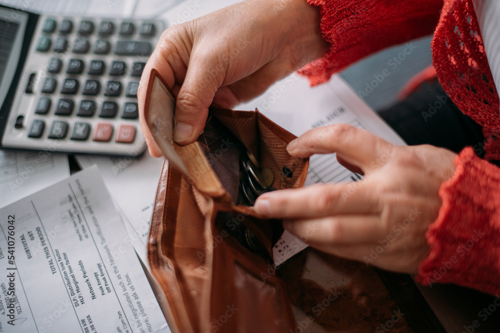 The hands of an elderly woman with an empty wallet and a lot of utility bills.