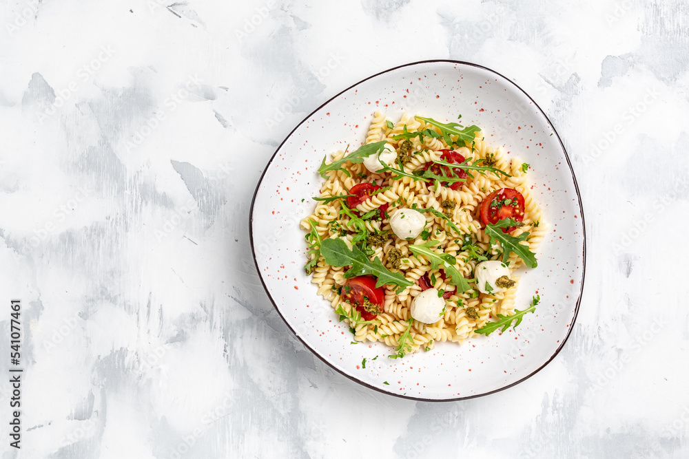 Italian cold pasta salad. Fusilli, tomato, mozzarella, olive, arugula. Pasta alla caprese on a dark background, Restaurant menu, dieting, cookbook recipe top view Italian cold pasta salad. Fusilli, tomato, mozzarella, olive, arugula. Pasta alla caprese on a dark background, Restaurant menu, dieting, cookbook recipe top view