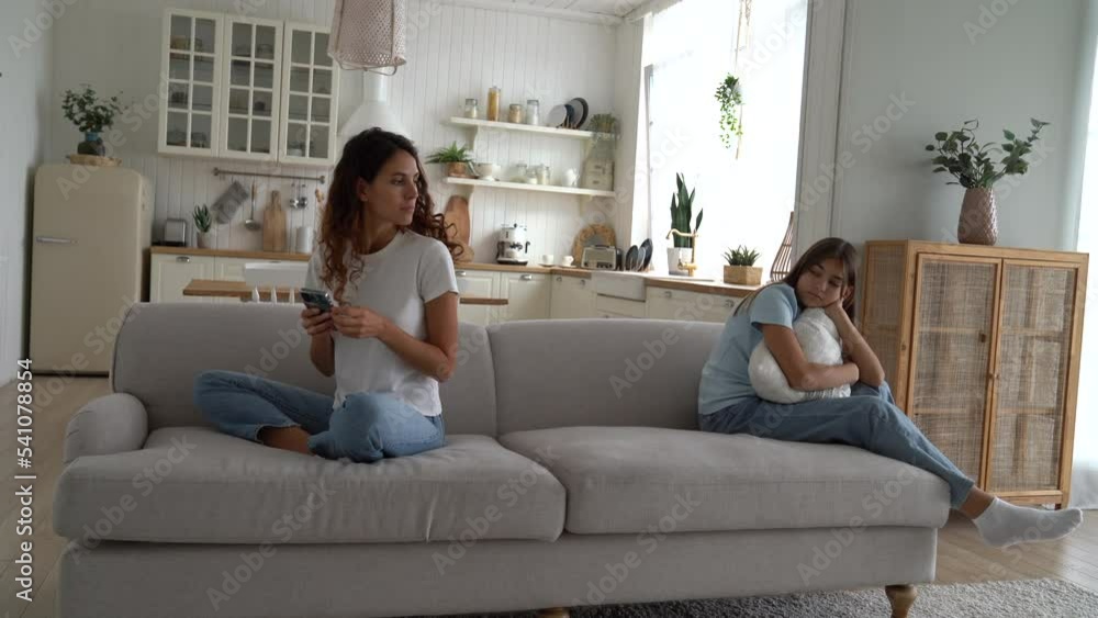 Dissatisfied mother and daughter sit on opposite sides of sofa with their backs turned experiencing mutual resentment. Family problems between woman and adopted teenage girl due to lack understanding Dissatisfied mother and daughter sit on opposite sides of sofa with their backs turned experiencing mutual resentment. Family problems between woman and adopted teenage girl due to lack understanding