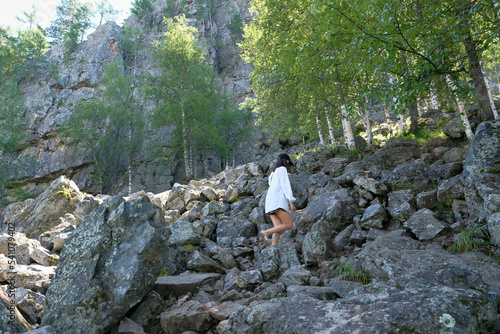 Girl tourist climbs the stones in the mountains. Forest, summer, day.