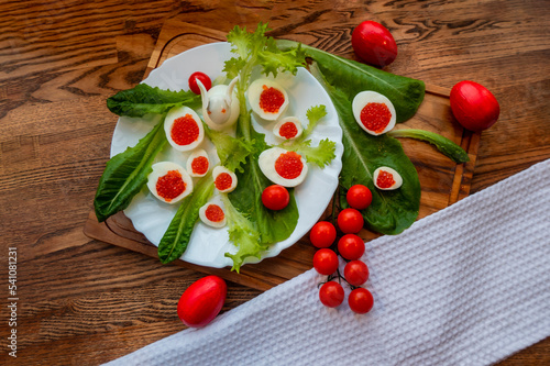 background of red caviar on dark wooden surface. edible egg rabbit figurine for decorating dishes easter dish decorated with red painted Easter eggs  cherry tomatoes and lettuce leaves