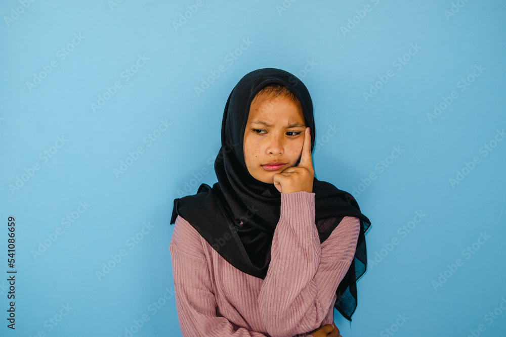 Portrait of thinking young Asian woman wearing hijab isolated on blue background Portrait of thinking young Asian woman wearing hijab isolated on blue background