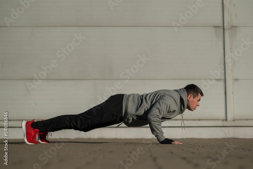 A man in a hoodie jumps while doing push-ups outdoors.