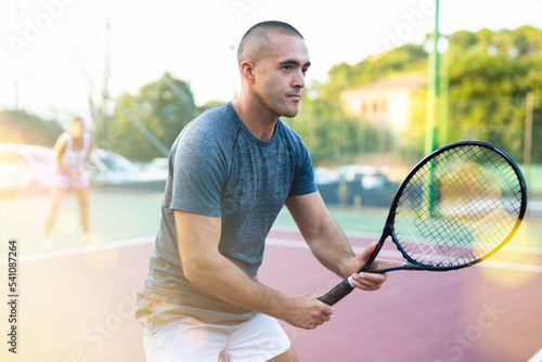 Man in t-shirt playing tennis on court. Racket sport training outdoors. © JackF