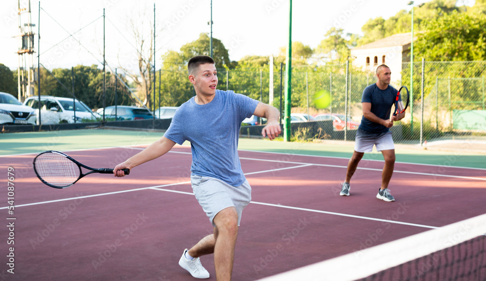 Sports active man during friendly doubles couple match. Two men playing together tennis outdoor