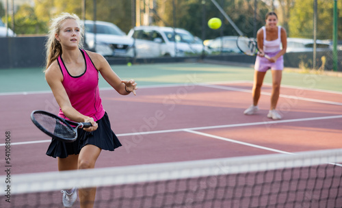 Sports active woman during friendly doubles couple match. Two women playing together tennis outdoors