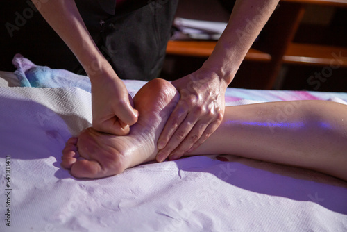 Detalhe de mãos de massoterapeuta fazendo massagem na sola do pé de paciente, com o uso de óleo essencial.