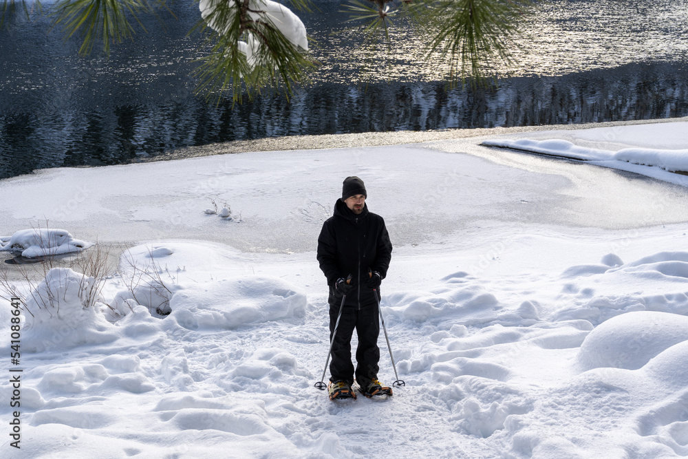 Man Snowshoeing Along Partly Frozen Lake in Winter