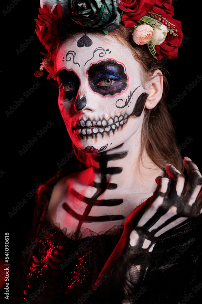 Female model wearing catrina skull body art and flowers crown, acting glamorous as santa muerte with halloween costume. Young adult with goddess of death holy mexican tradition. Female model wearing catrina skull body art and flowers crown, acting glamorous as santa muerte with halloween costume. Young adult with goddess of death holy mexican tradition.
