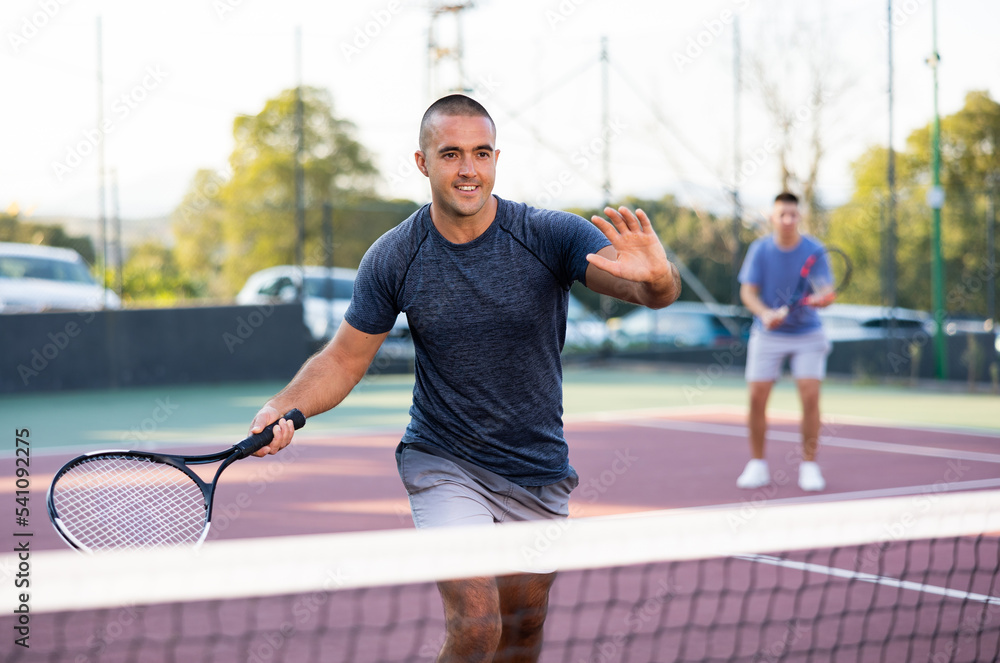 Young man and his male partner playing tennis on court during friendly match outdoor