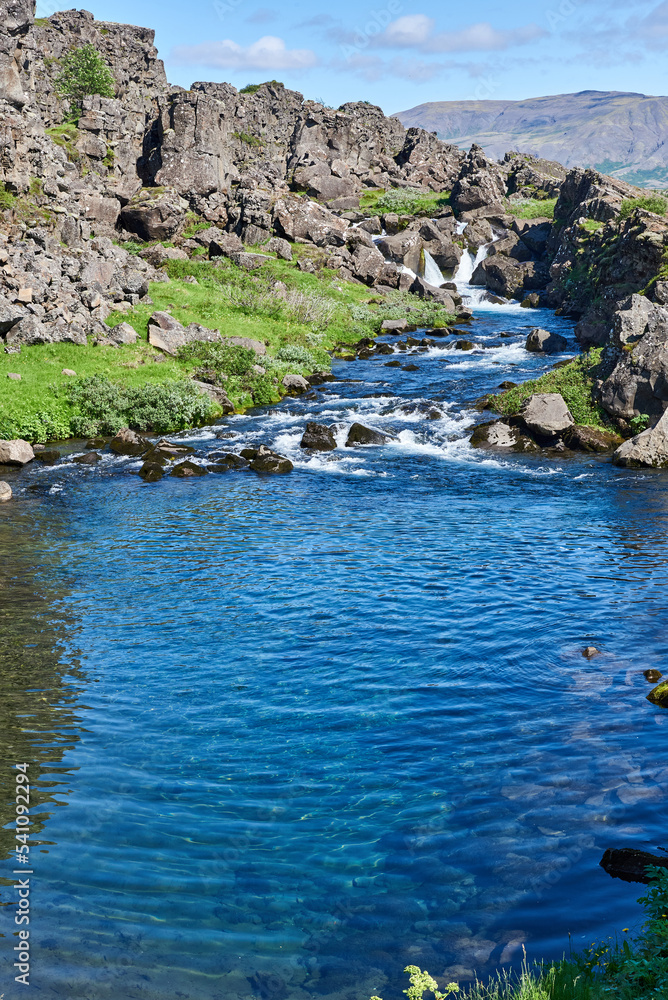 A view of the blue clear water of Drekkingarhylur (Drowning Pool) as it sits alongside the rock walls of Almannagja Fault in Thingvellir National Park, Iceland.