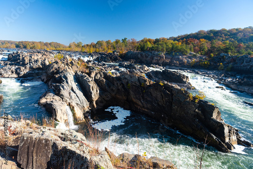 Autumn view of the mountain river. Stormy water flows among high stones and rocks under a blue sky