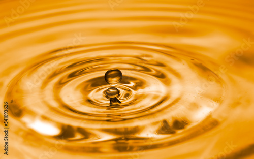 Water droplets flowing on water surface created ripples texture with golden light effects background.