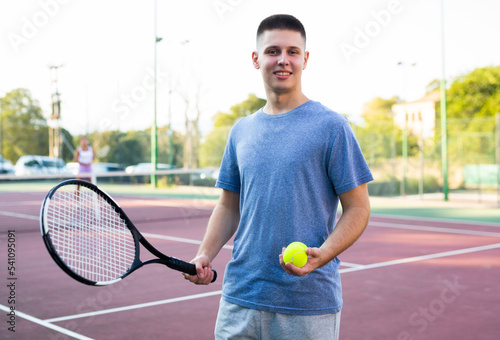 Portrait of positive caucasian boy standing on tennis court, holding racket and ball. © JackF