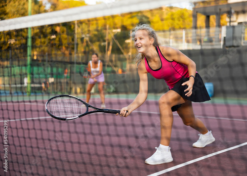 Sportive woman in shorts and t-shirt playing tennis on court. View through the tennis net